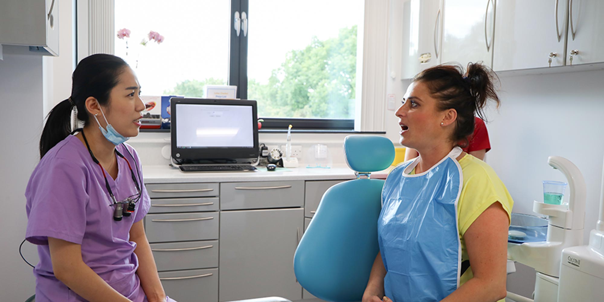 patient sitting in blue dental chair speaking with dentist